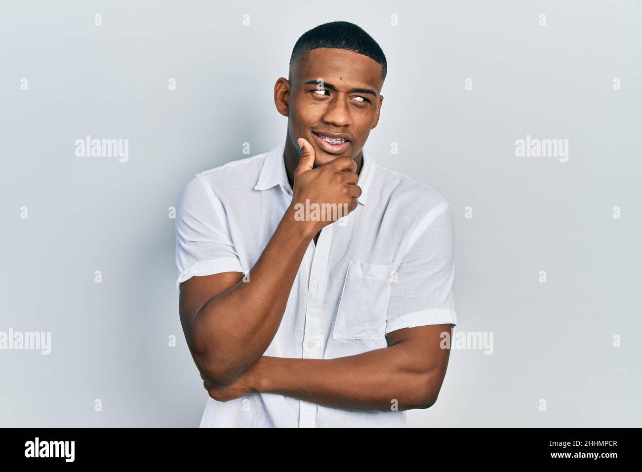 Young black man wearing casual white shirt with hand on chin thinking ...