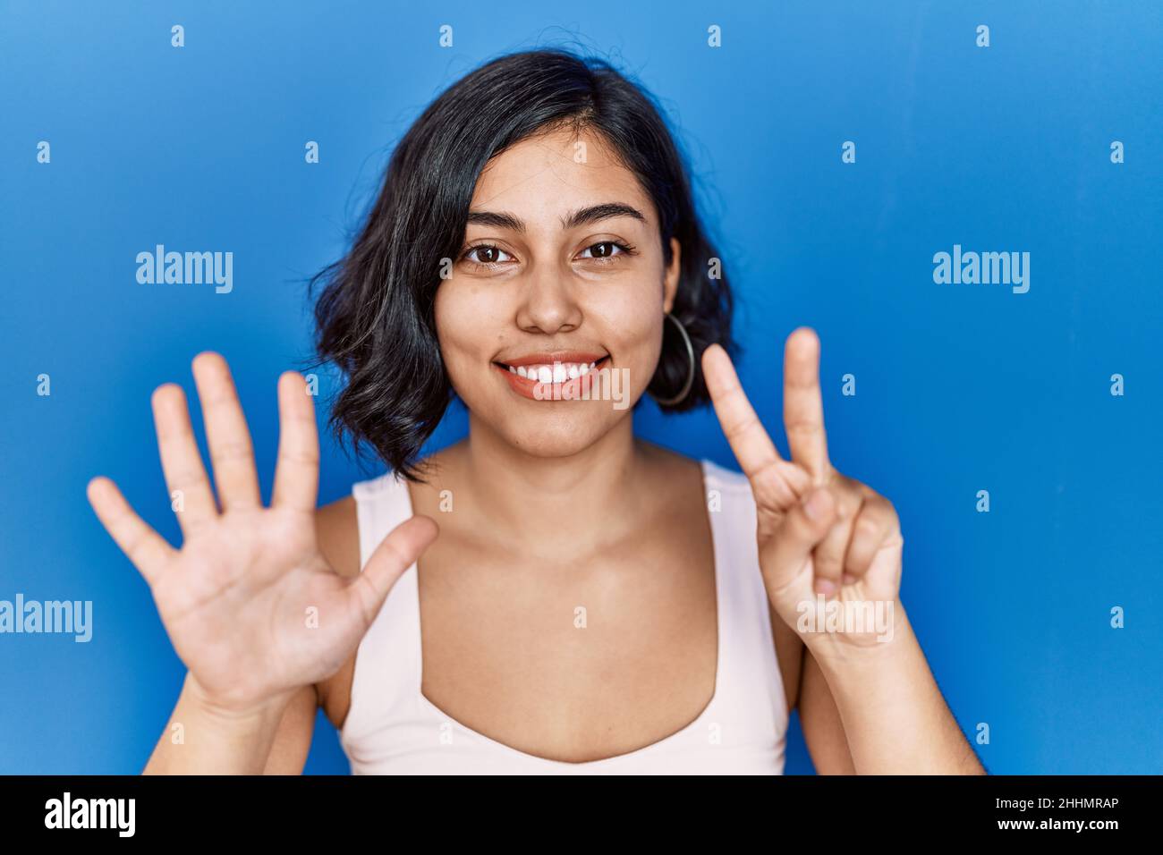 Young hispanic woman standing over blue background showing and pointing ...