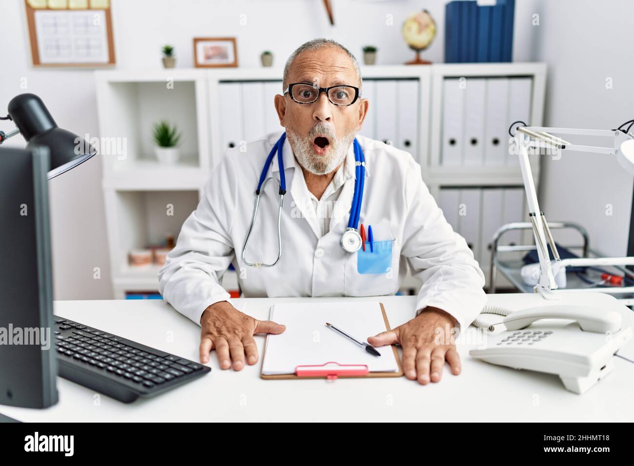 Mature doctor man at the clinic afraid and shocked with surprise ...