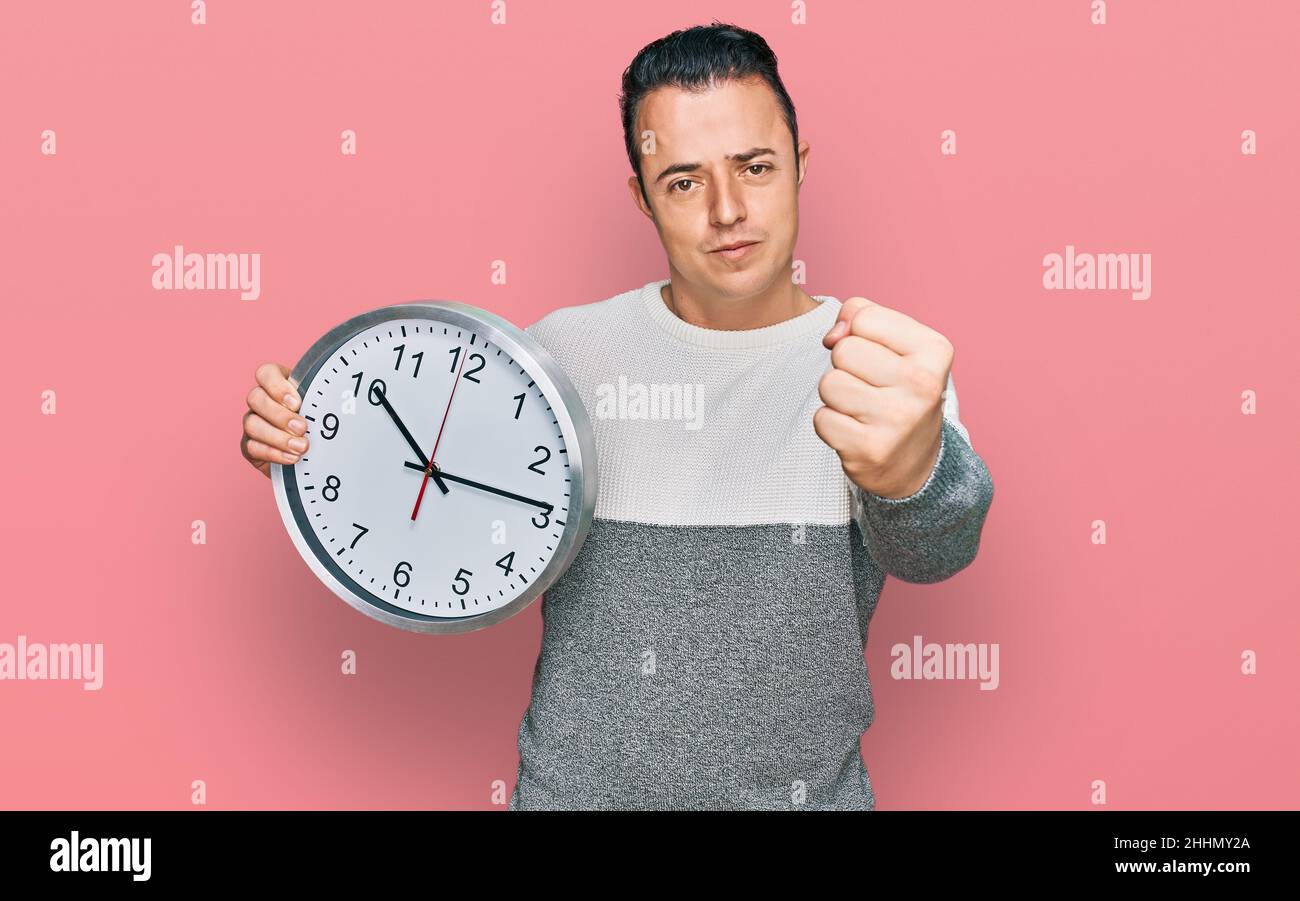 Staring At Clock Rage Handsome young man holding big clock annoyed and frustrated shouting ...