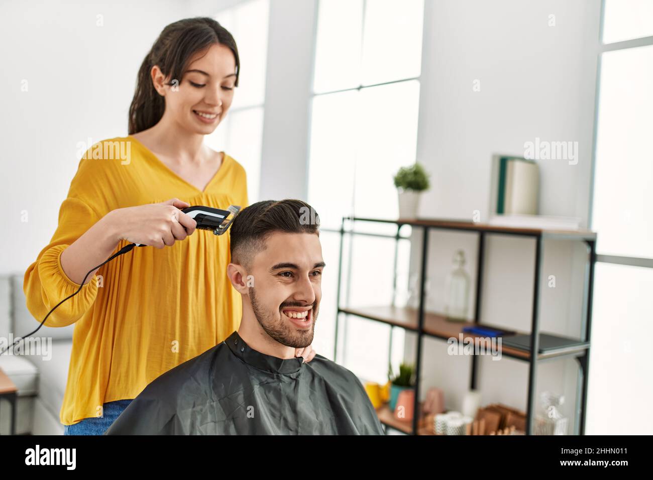 Young hispanic hairdresser woman cutting man's hair using electric ...