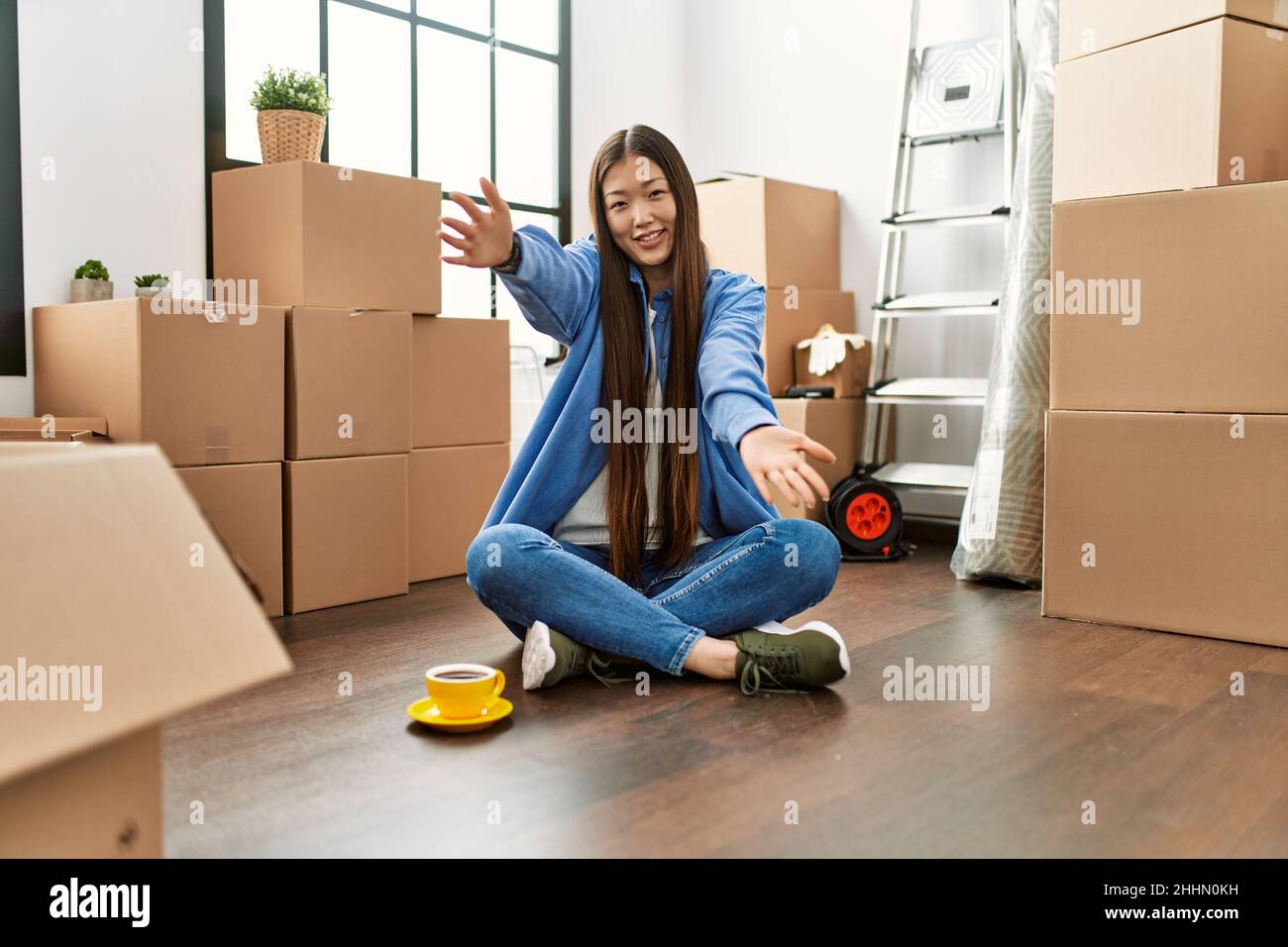 Young chinese girl sitting on the floor at new home looking at the ...