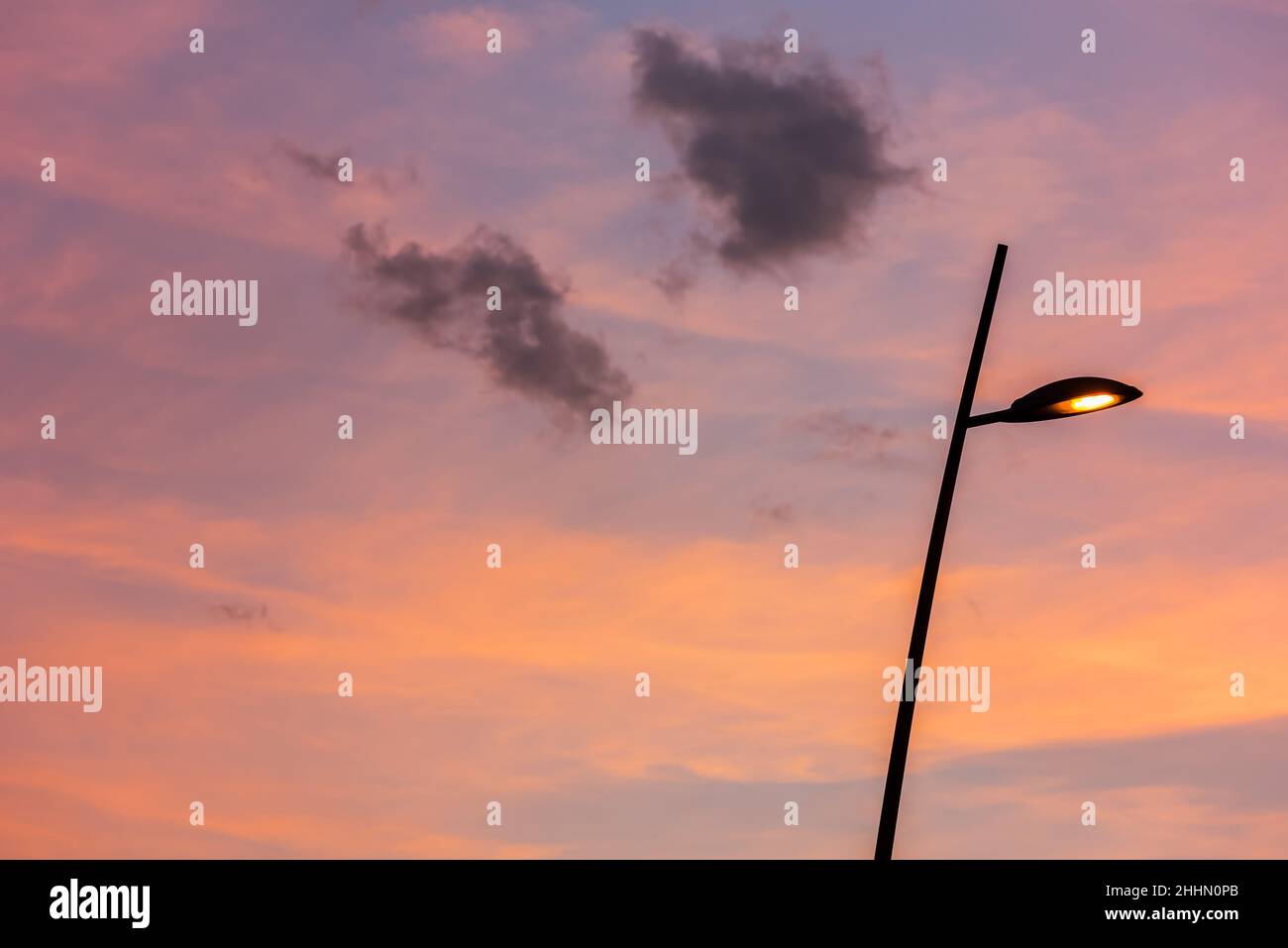 Street lamp silhouetted against an orange sunset sky with lilac colored clouds in a full frame background Stock Photo