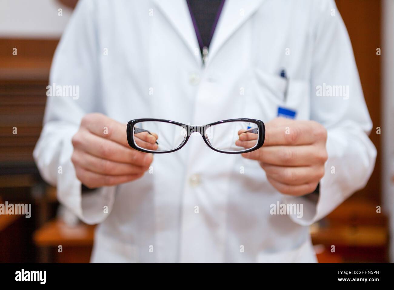 A male eye doctor in a white coat shows a pair of corrective eyeglasses