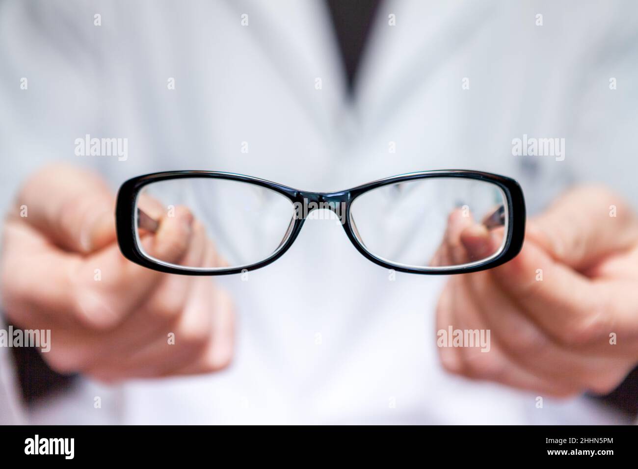 An optician in a white coat shows a pair of corrective eyeglasses to