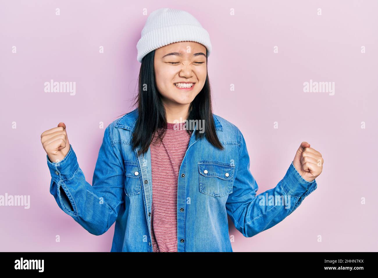 Young chinese girl wearing cute wool cap very happy and excited doing winner gesture with arms raised, smiling and screaming for success. celebration Stock Photo