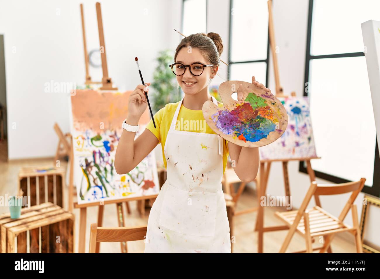 Adorable girl smiling confident holding paintbrush and palette at art ...