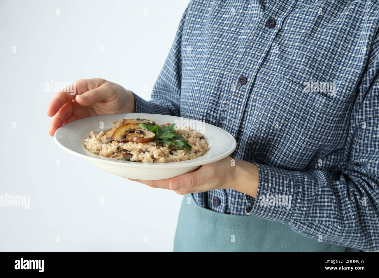 Woman in apron holds plate of risotto with mushrooms Stock Photo