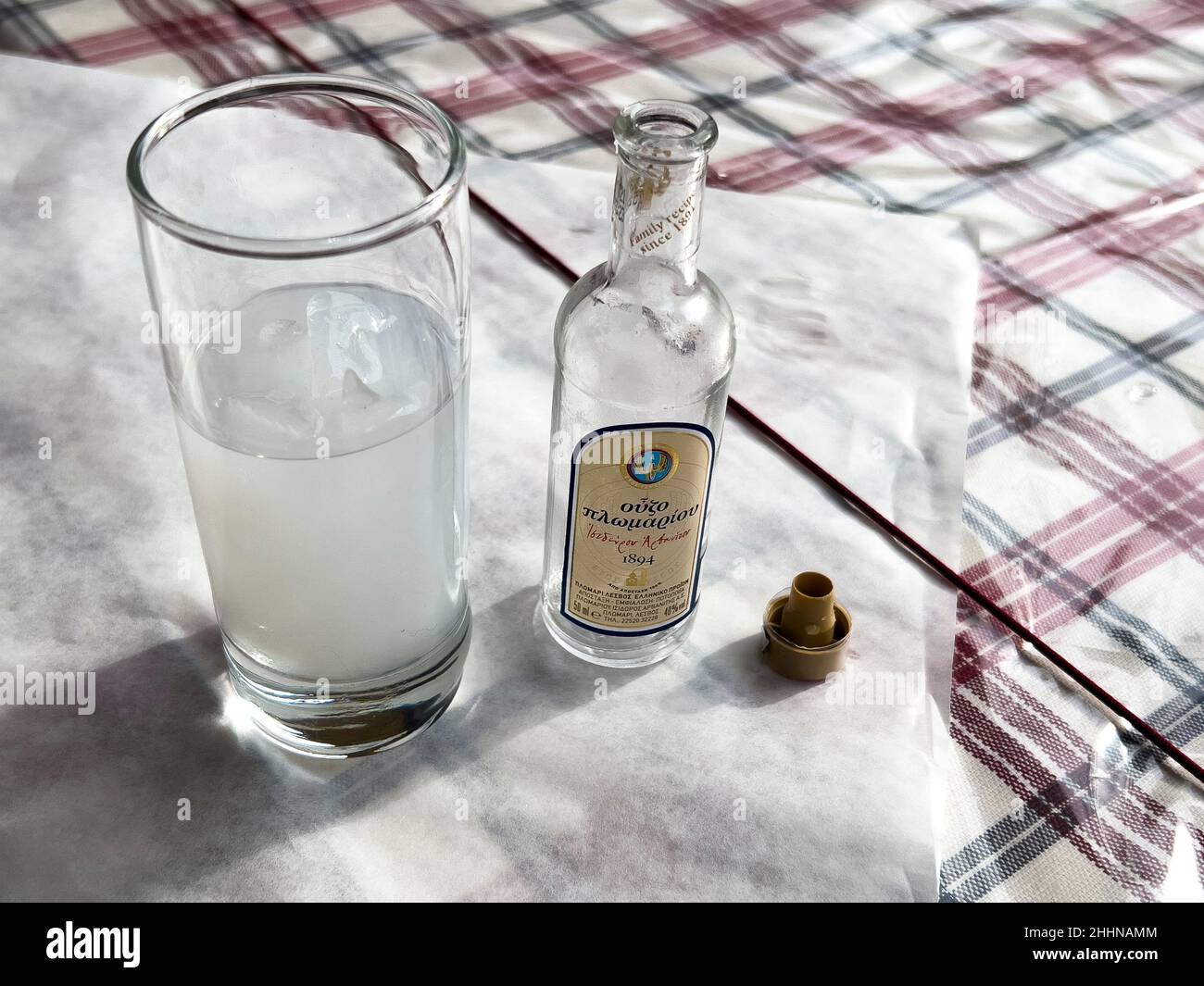ATHENS, GREECE - JANUARY 16, 2022: Greek spirit Ouzo of Plomari branded bottle. Aperitif liquor drink with anise flavored milky liquid in glass. Stock Photo