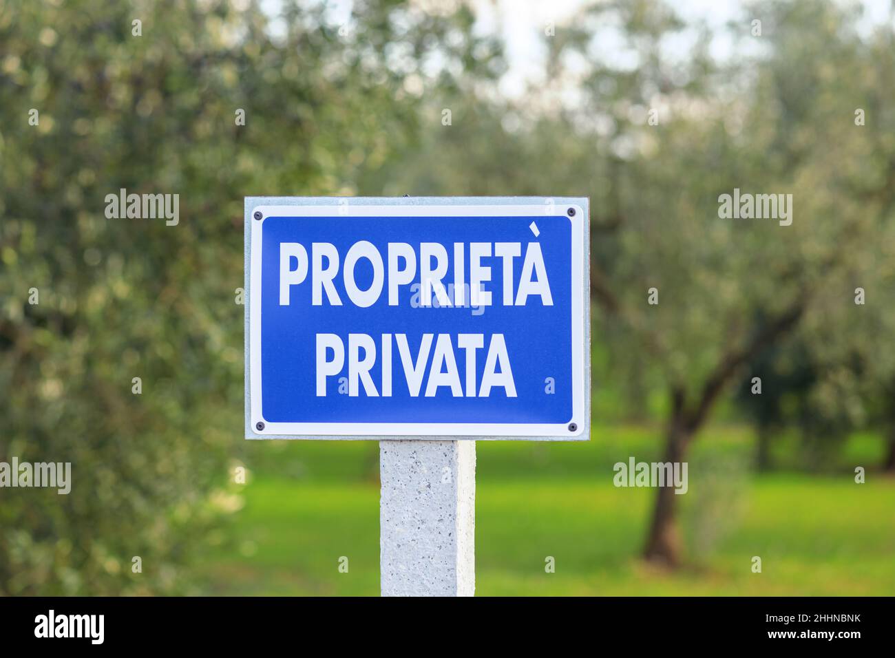 Blue sign with the inscription Private property in Italian outdoor in olive grove with olive trees blurred background Stock Photo