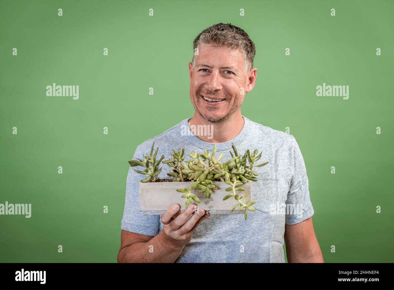 portrait of man who is holding a green plant in front of a green ...