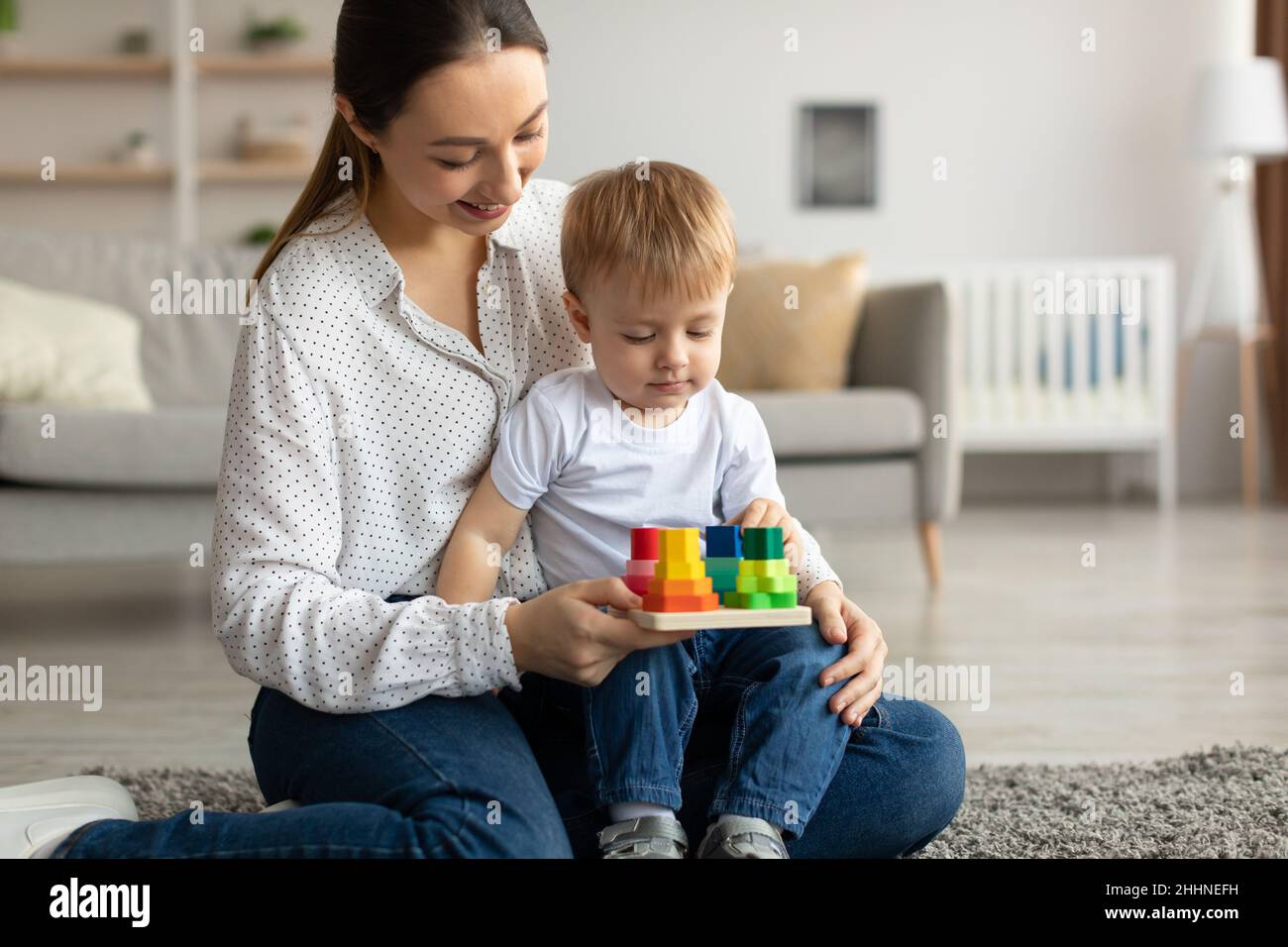 Young mom and her toddler son playing with educational toys, boy engaged in interesting development game Stock Photo