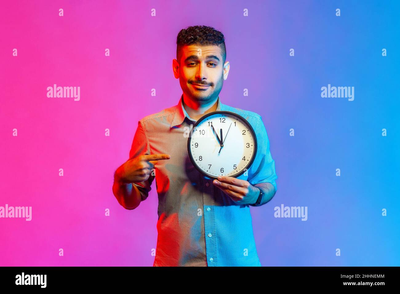 Look at time. Portrait of handsome positive man in shirt pointing big ...
