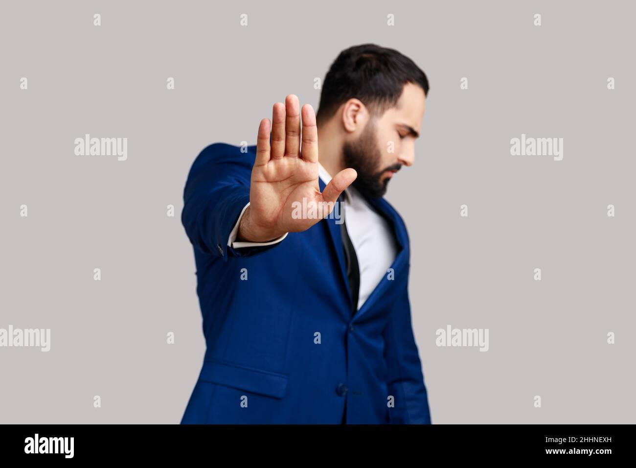 Bearded man making stop gesture showing palm of hand and turning head aside, conflict prohibition warning about danger, stop bullying. Indoor studio shot isolated on gray background. Stock Photo