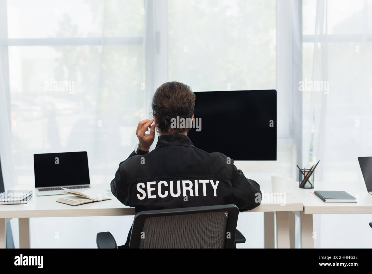back view of security man in black uniform and earphone sitting near ...