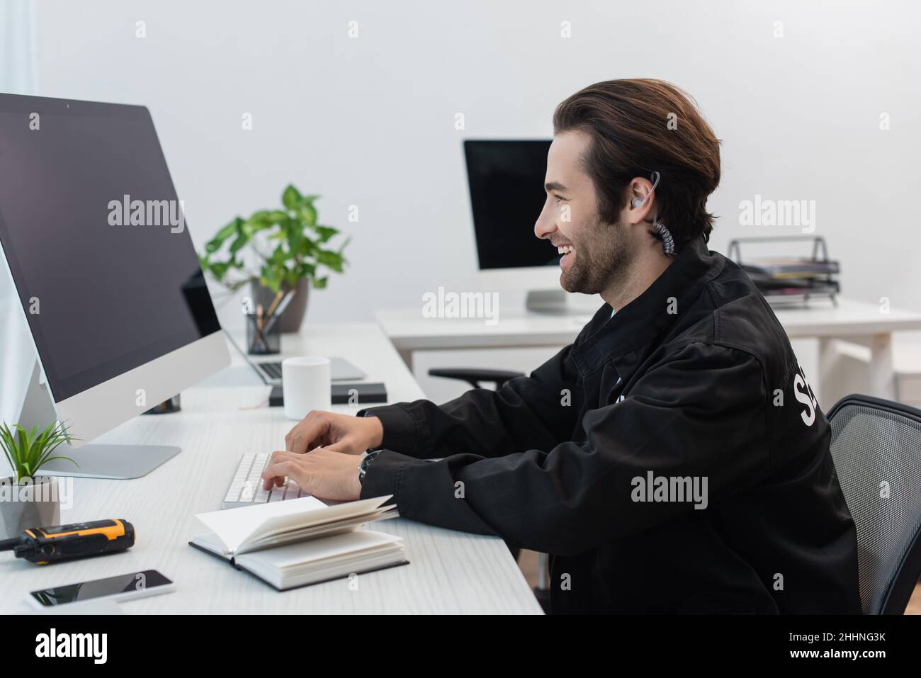 Security Man At Computer side view of smiling security man typing on computer near notebook and ...