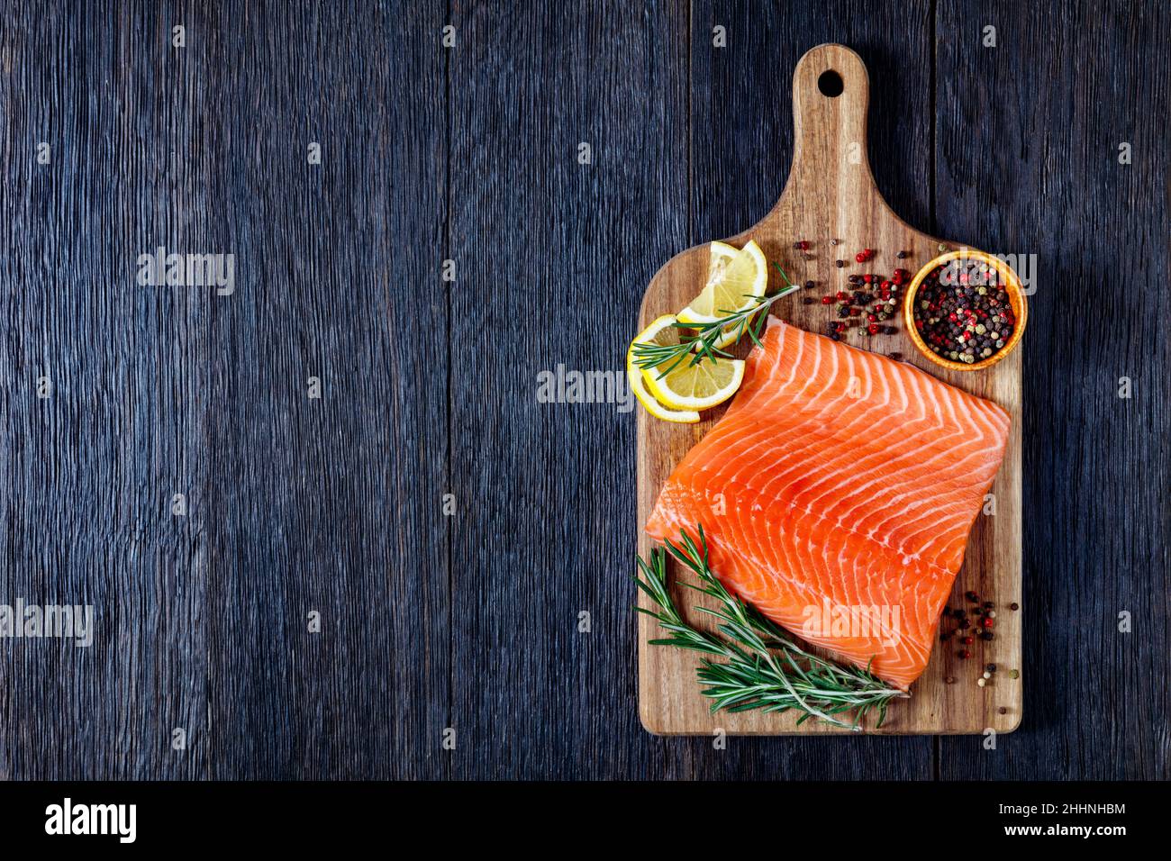 salmon fillet with pepper, rosemary and lemon on wooden cutting board ...