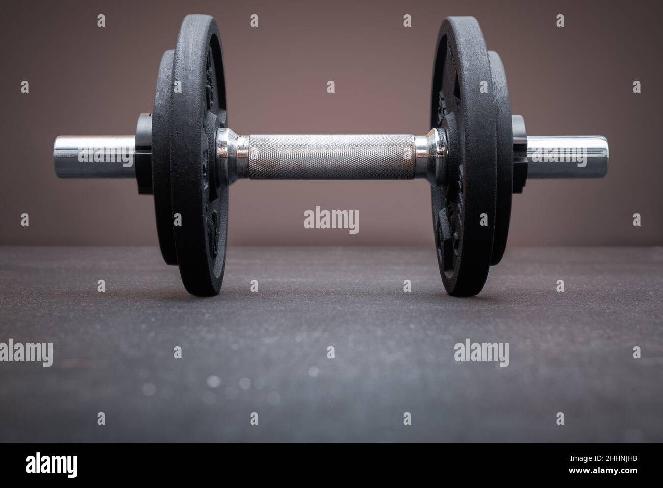 A dumbbell bar loaded with weight plates on the floor at the gym. Bodybuilding equipment on a clean background with empty space for text Stock Photo