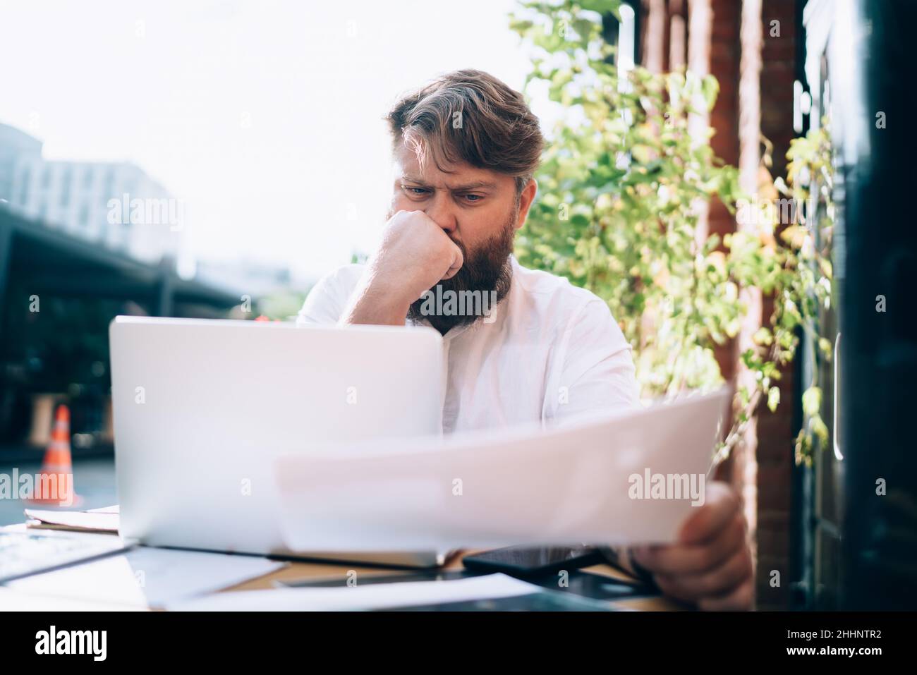 Thoughtful man working on project with documents and laptop Stock Photo