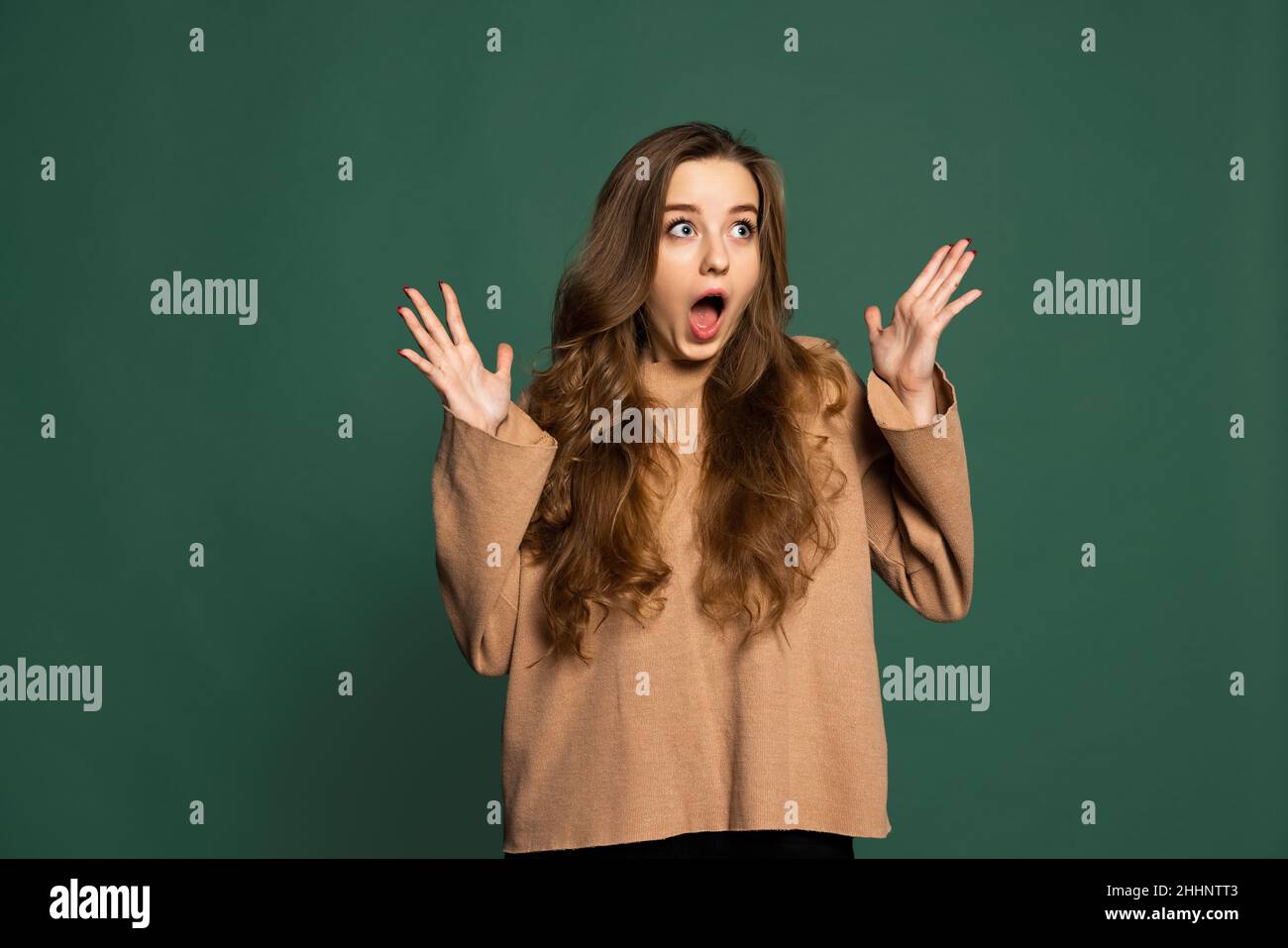 Surprised young beautiful girl wearing brown sweatshirt isolated on green background. Concept of emotions, facial expression Stock Photo