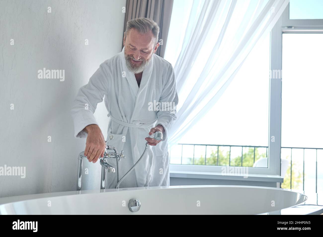 Smiling contented mature male filling the bath with water Stock Photo