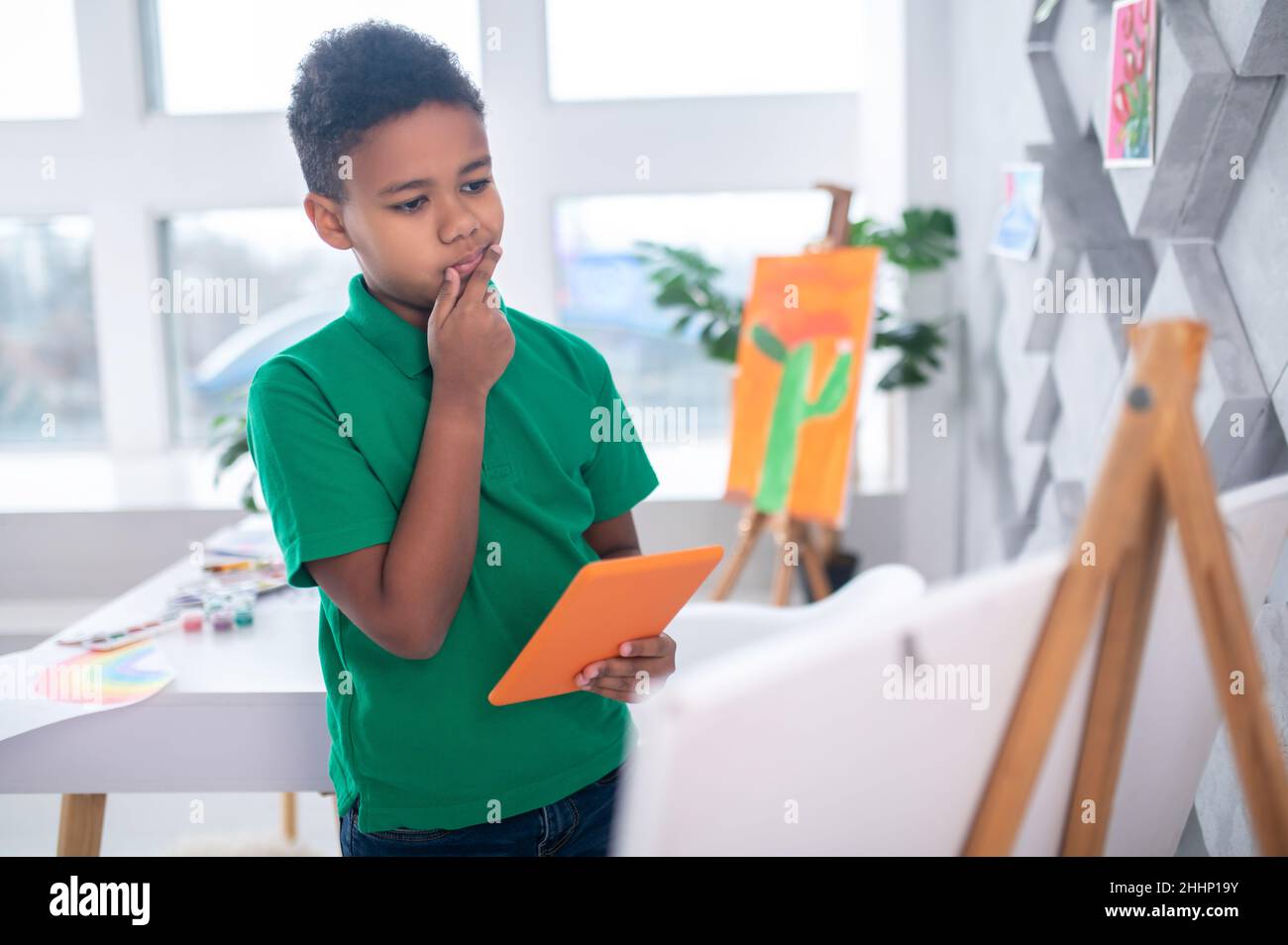Boy with tablet looking thoughtfully at drawing easel Stock Photo Alamy