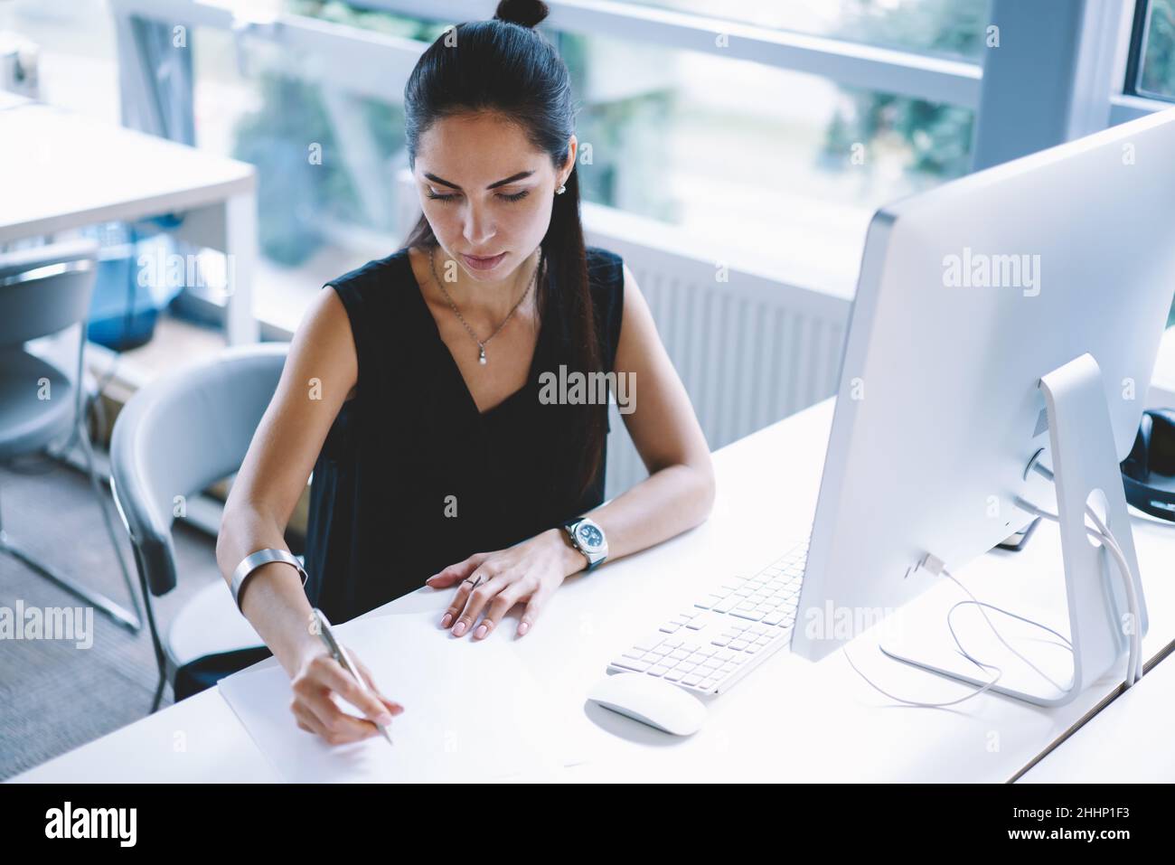 Businesswoman taking notes while working in modern workspace Stock Photo