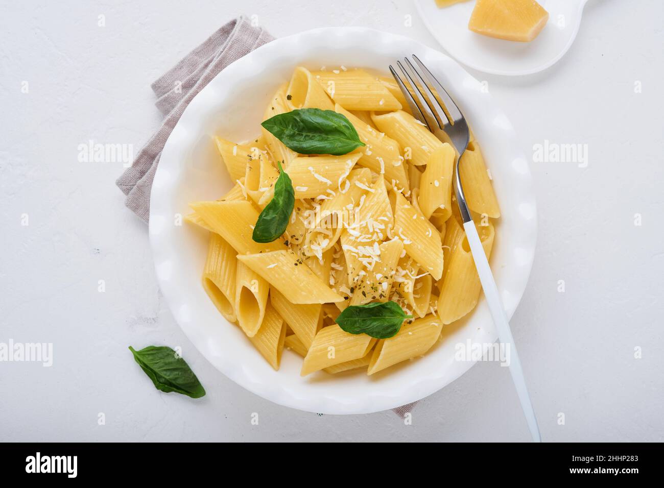 Tasty appetizing classic italian penne pasta with parmesan cheese and basil in white plate on plate on on stone table. Traditional dish of Italian cui Stock Photo