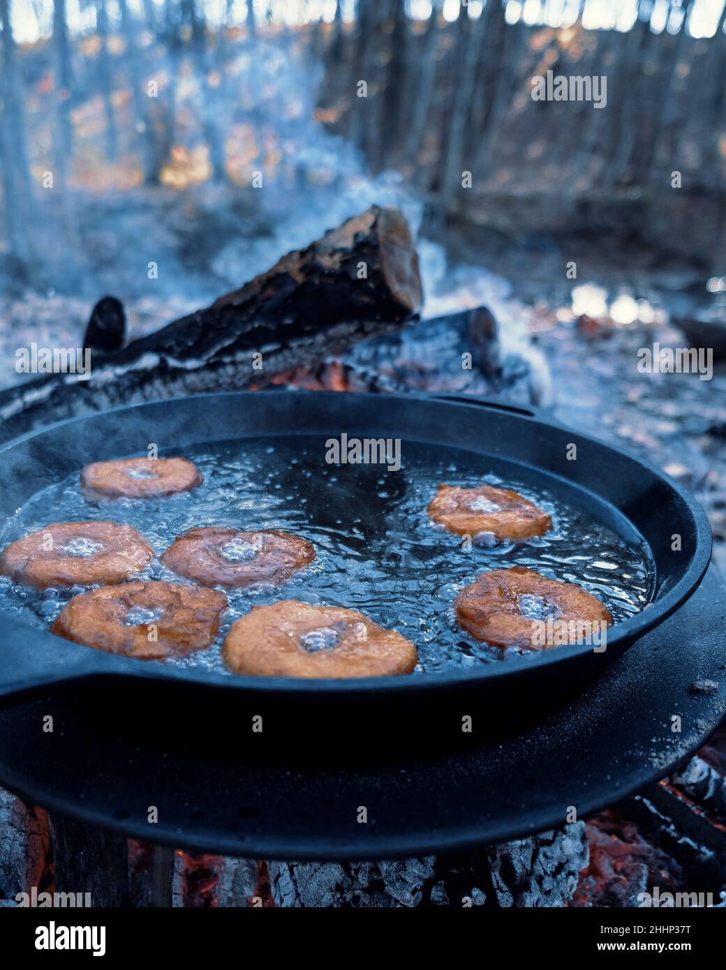 Homemade donuts frying in cast iron skillet outdoors at campsite Stock