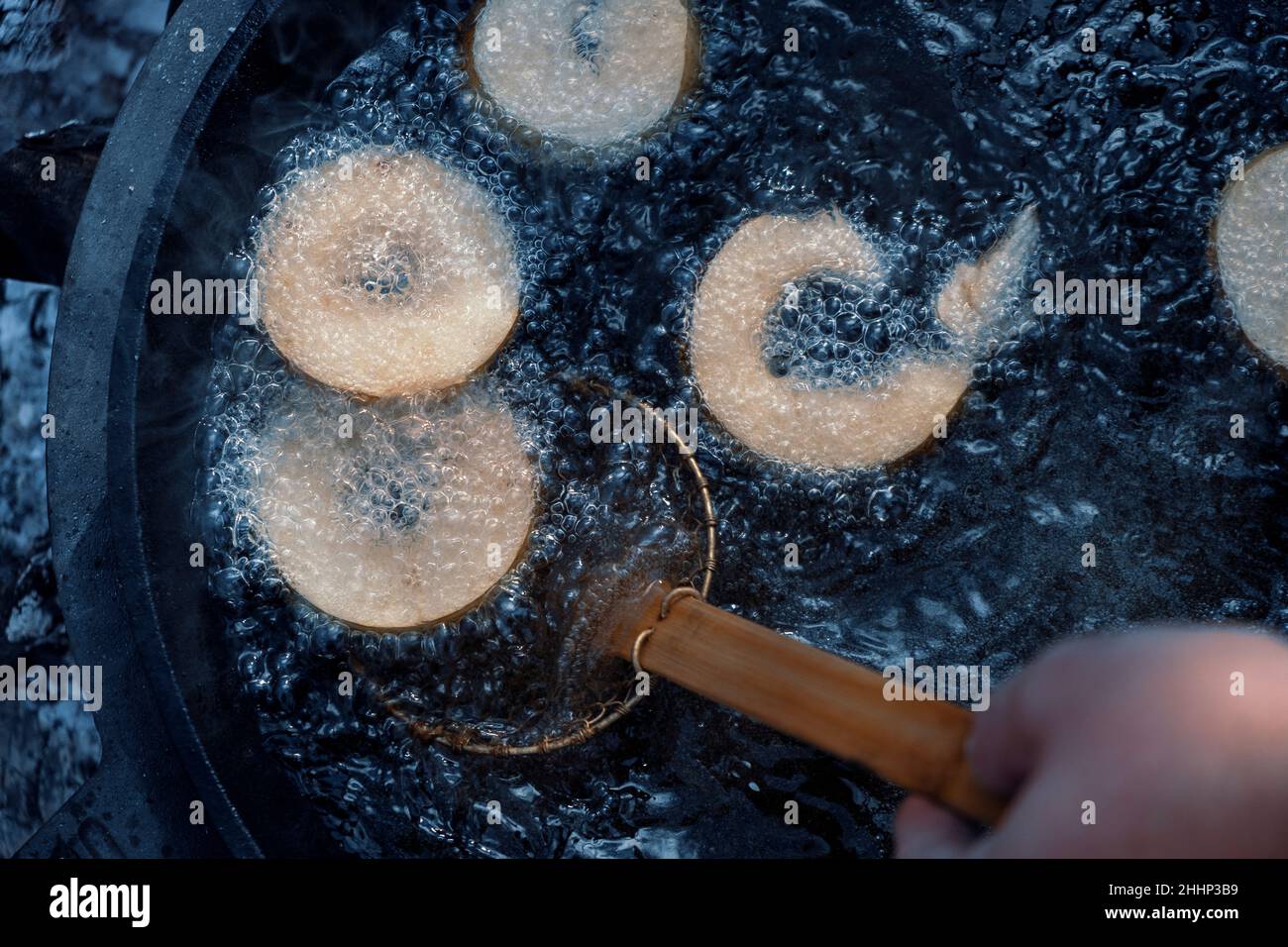 Homemade donuts frying in cast iron skillet outdoors at campsite. Stock Photo