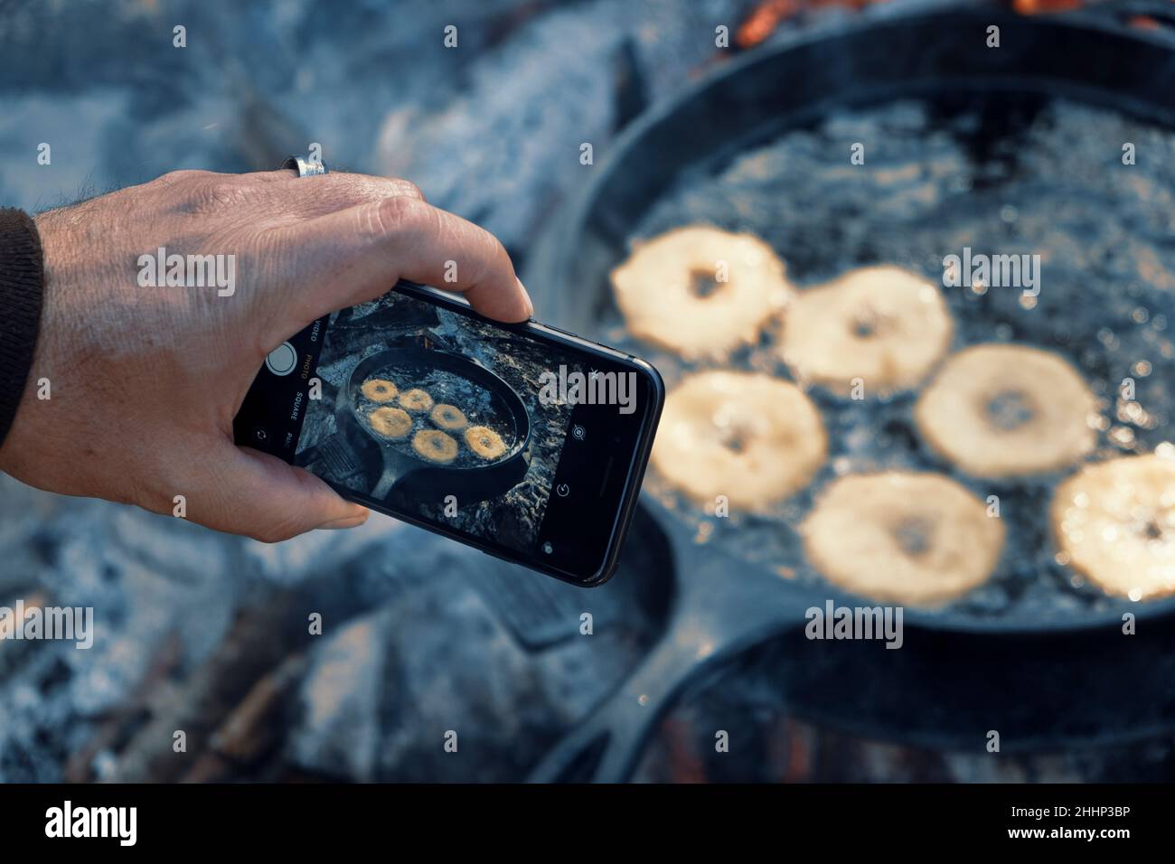 Taking a photo of Homemade donuts frying in cast iron skillet outdoors at campsite. Stock Photo
