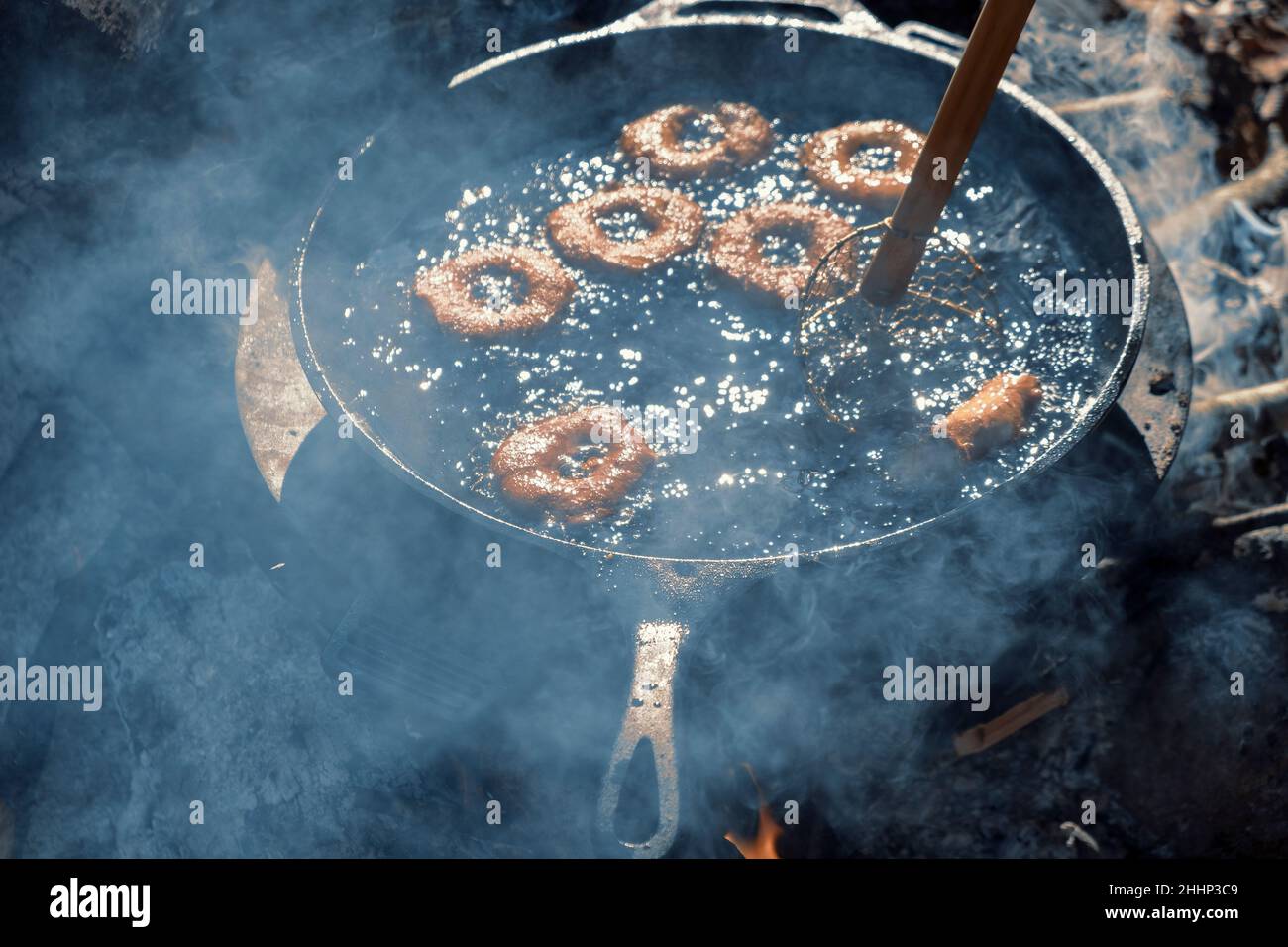 Homemade donuts frying in cast iron skillet outdoors at campsite. Stock Photo