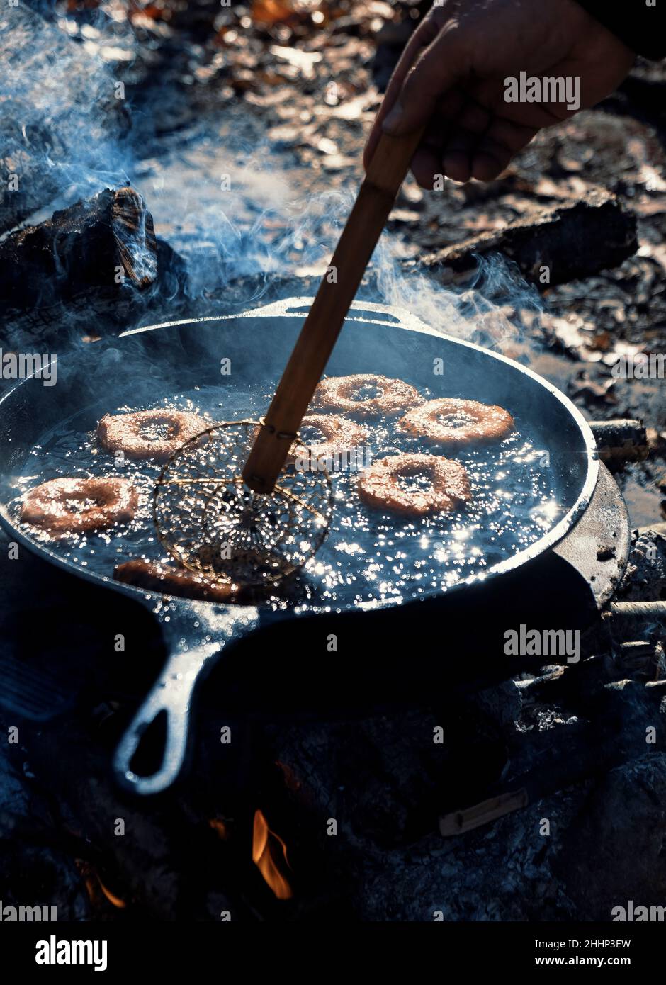 Homemade donuts frying in cast iron skillet outdoors at campsite Stock