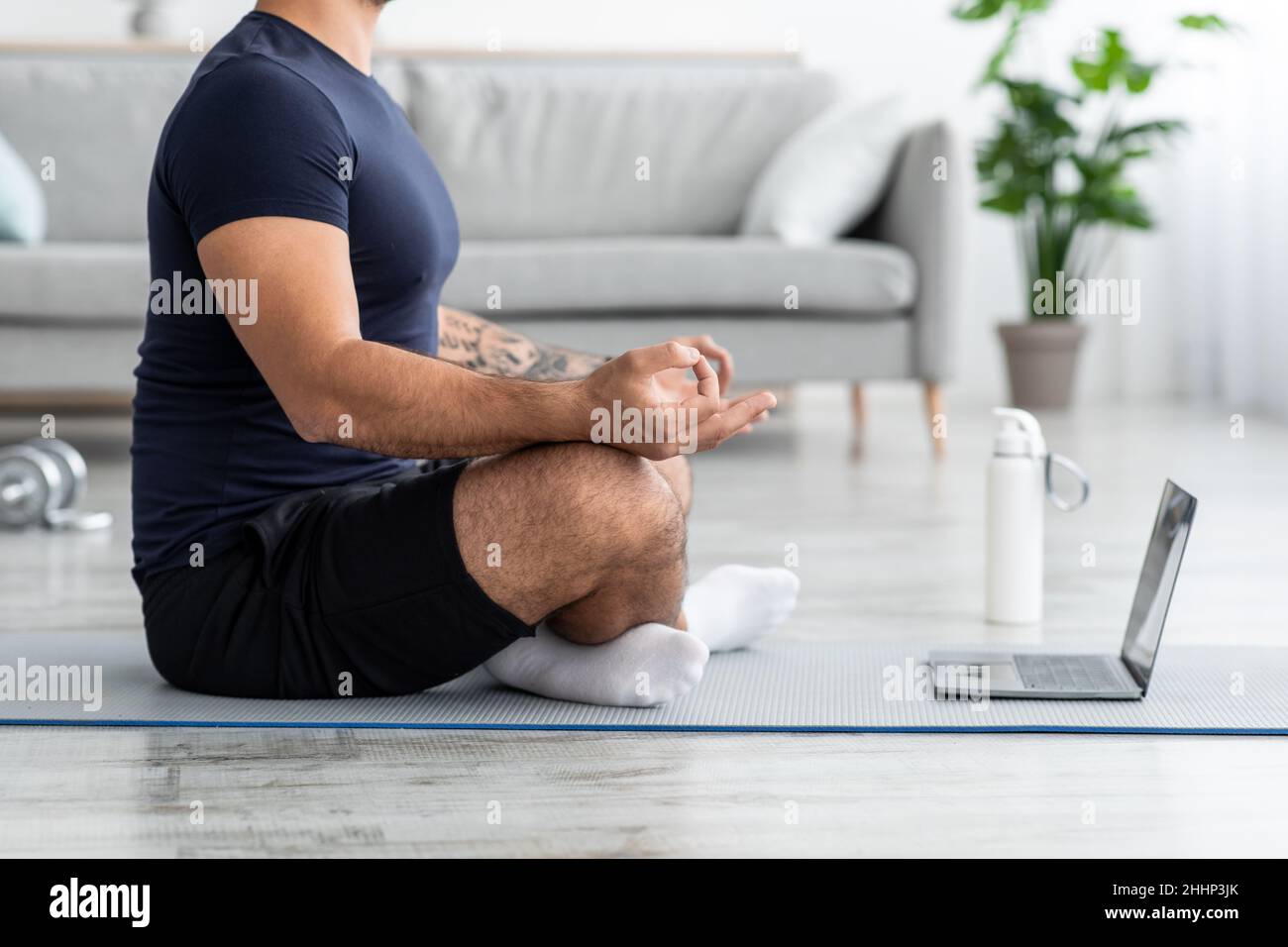 Millennial european muscular man meditating in lotus position, sits on  floor on mat with laptop in living room Stock Photo - Alamy