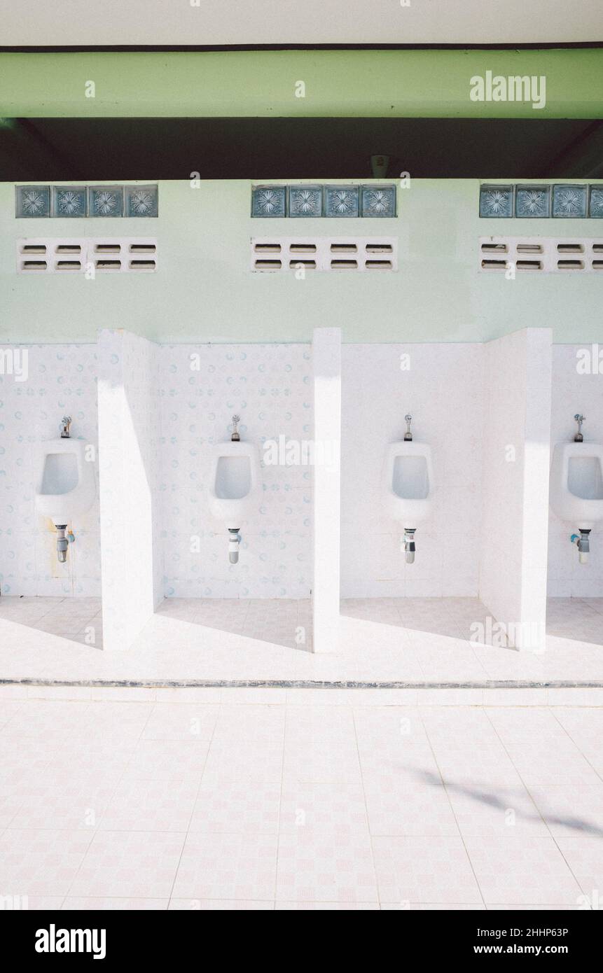 Vertical shot of white urinals separated by walls in a public bathroom
