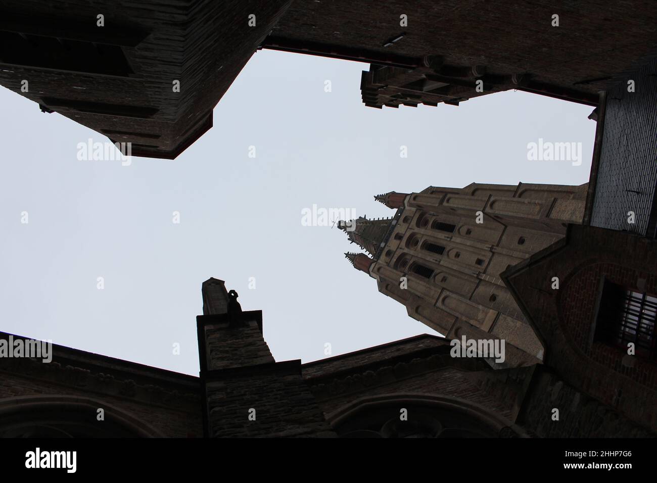 Looking up through medieval buildings at the steeple of the Church of Our Lady (Bruges, Belgium). Bruges skyline. Abstract city view. Claustrophobic. Stock Photo
