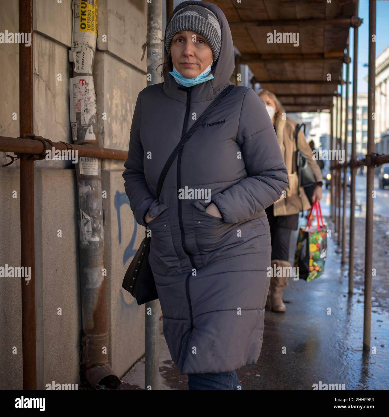 Belgrade, Serbia, Jan 23, 2022: A hooded woman walking down the street under scaffolding placed above the sidewalk Stock Photo