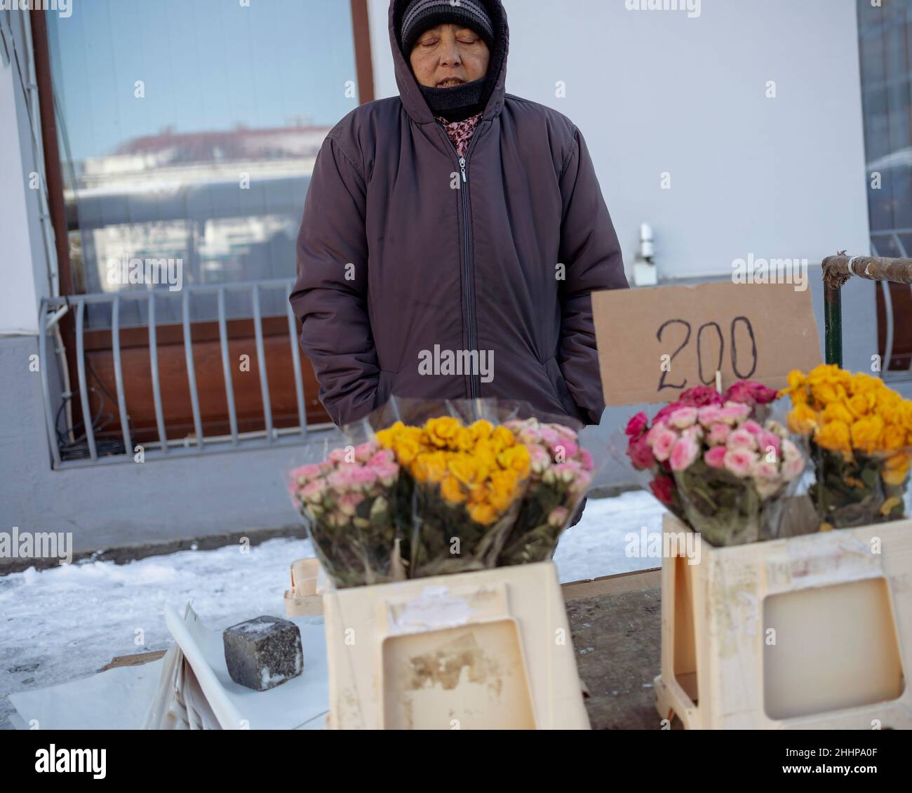 Belgrade, Serbia, Jan 23, 2022: A hooded female street vendor standing next to stall with flowers and freezing Stock Photo
