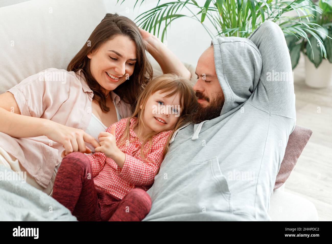 Happy family Mother father and daughter lie in bed rest hugging and having fun Play Tickle. Parenting in Morning routine, Family awakening. Daytime Stock Photo