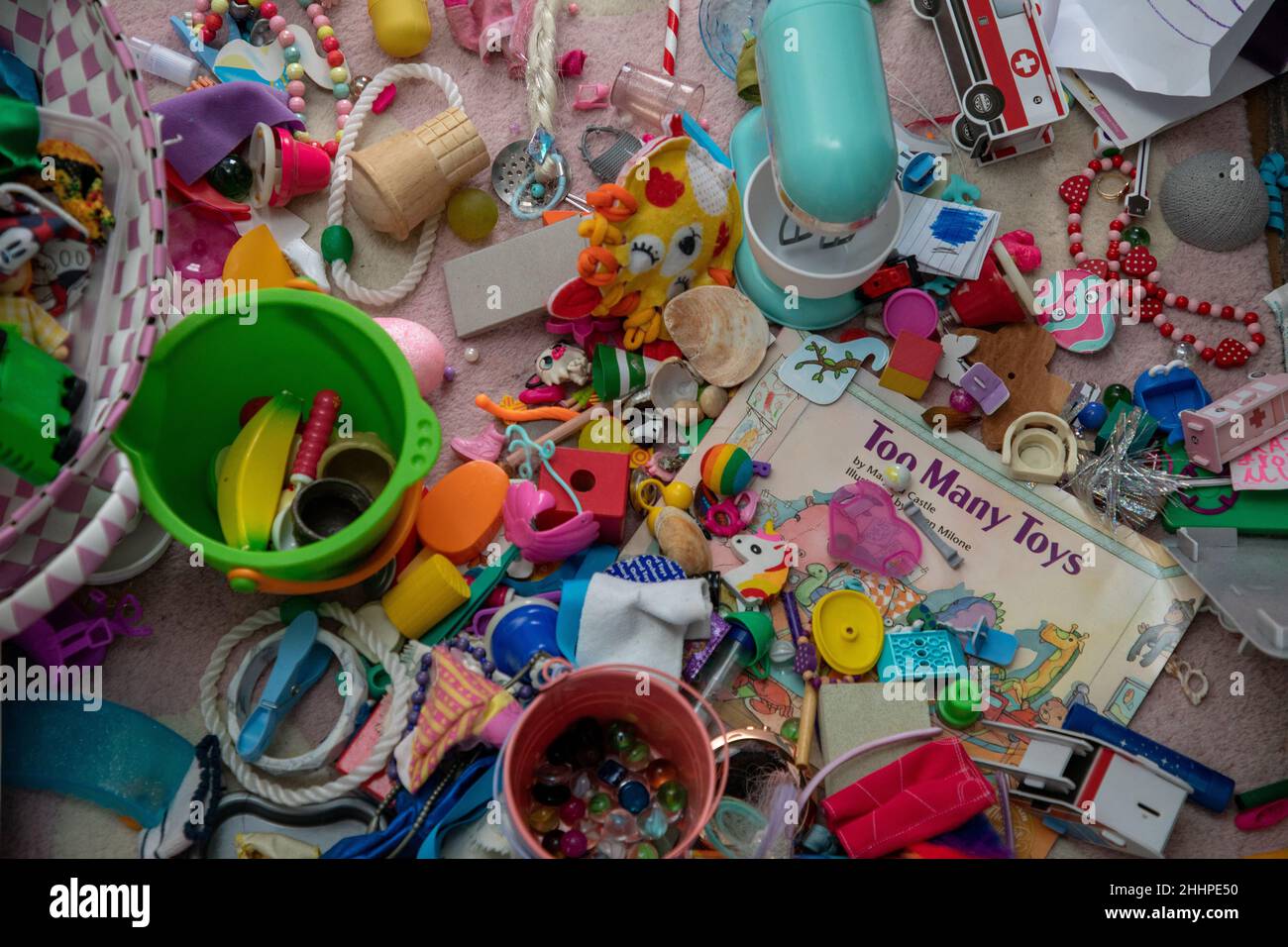 Assorted miscellaneous small children’s toys on a carpet and a book entitled 'Too Many Toys' Stock Photo