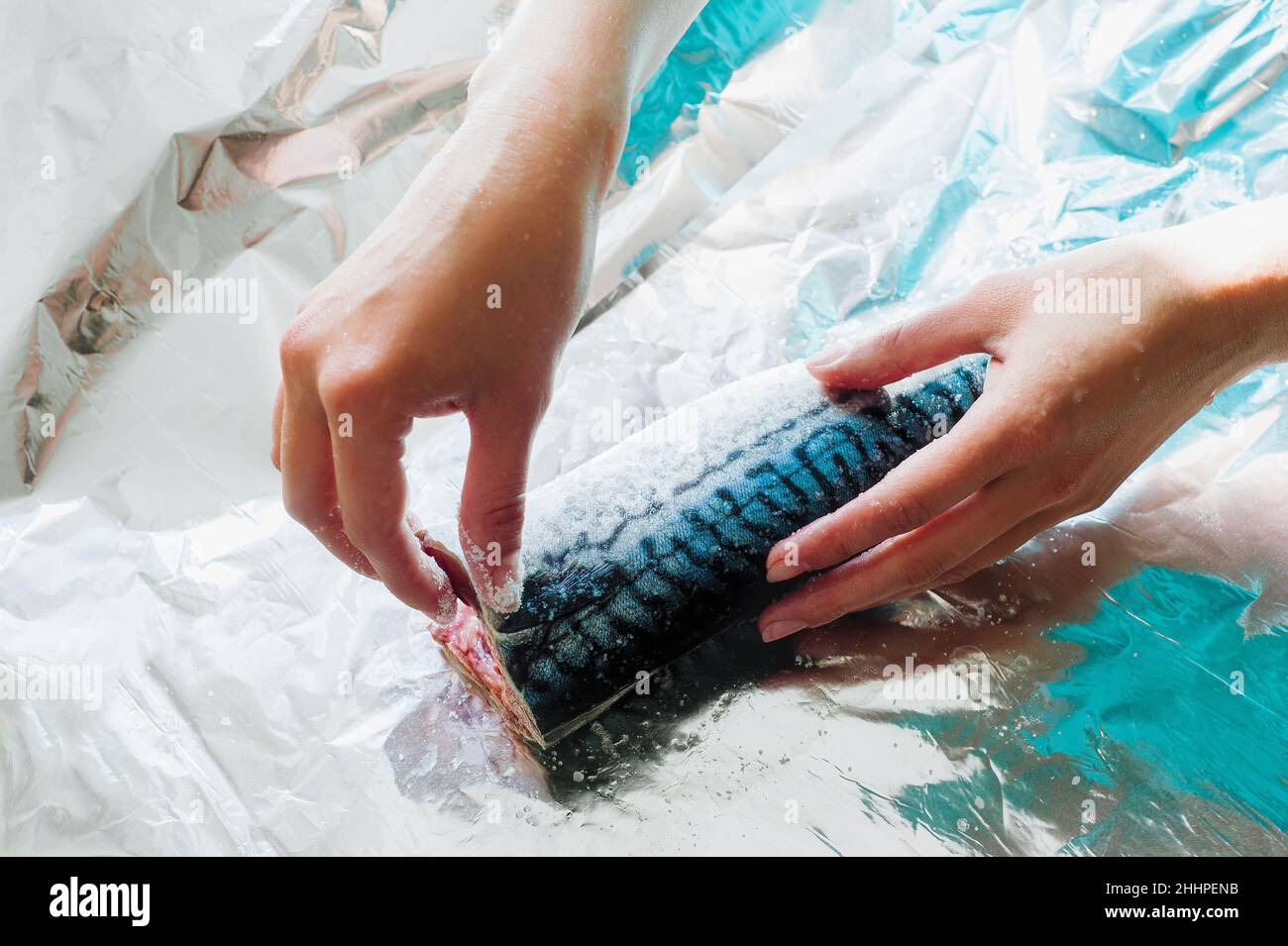 Woman marinate raw mackerel. Fresh fish with sea salt lie on a shiny