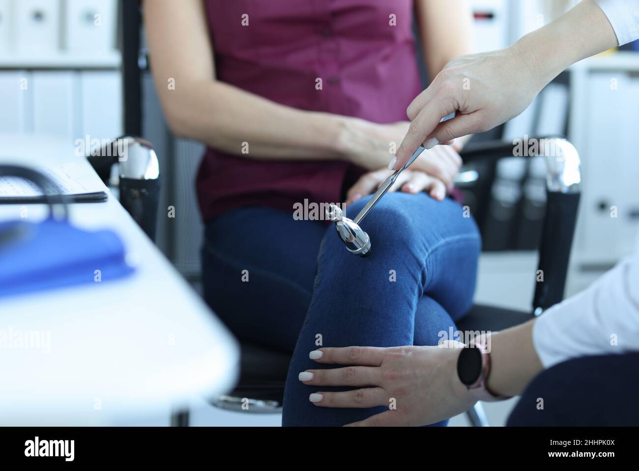 Doctor neurologist knocking on knee of patient with hammer in clinic closeup Stock Photo