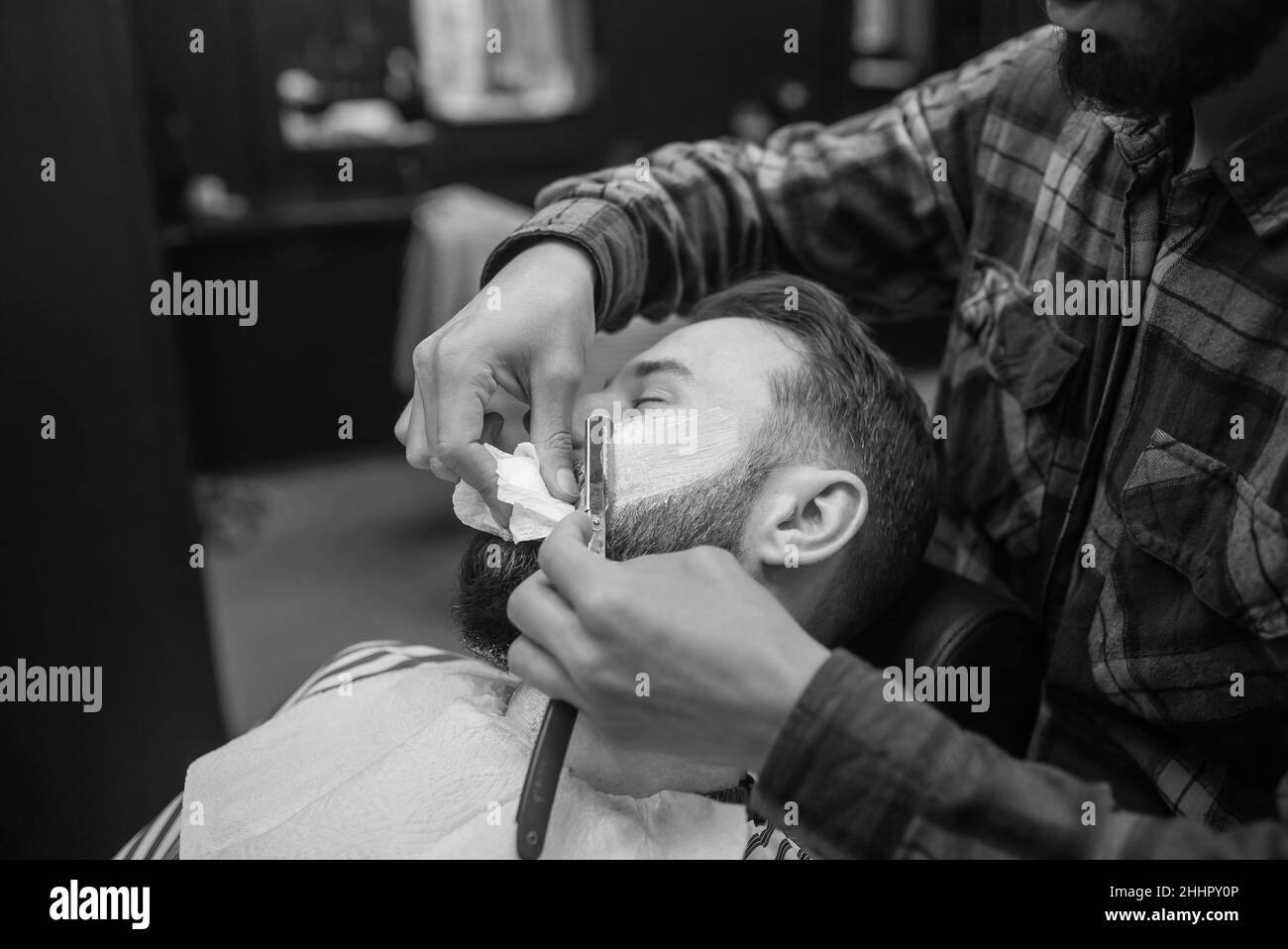 Young bearded man getting shaved by hairdresser at barbershop Stock Photo