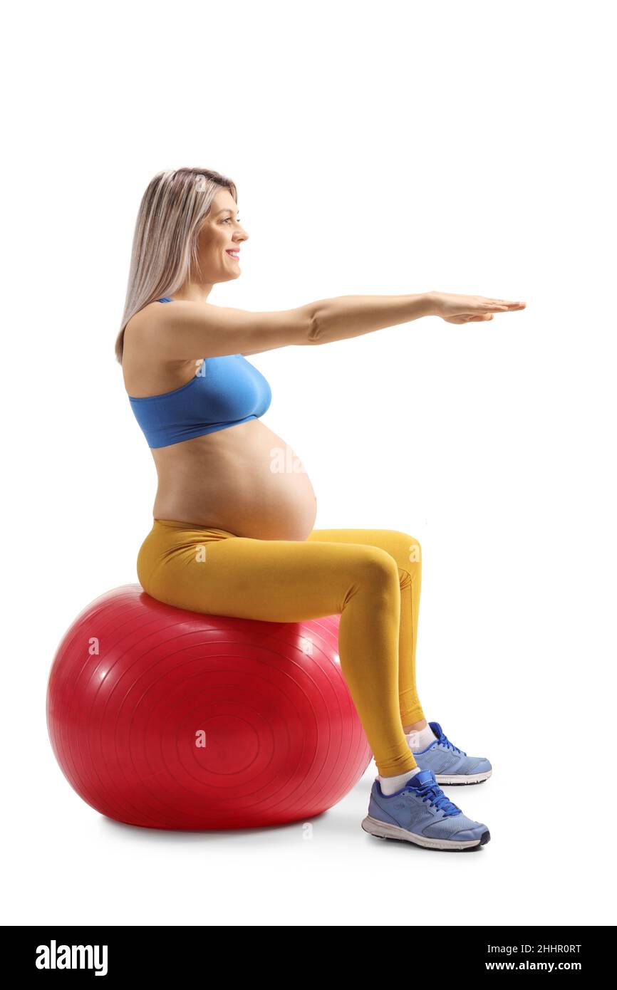 Full length profile shot of a pregnant woman in a crop top sitting on a fitness ball and exercising isolated on white background Stock Photo
