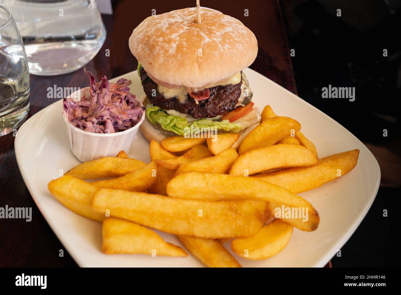Juicy beef inside a gourmet beef burger stack on a white plate with chunky chips and a small