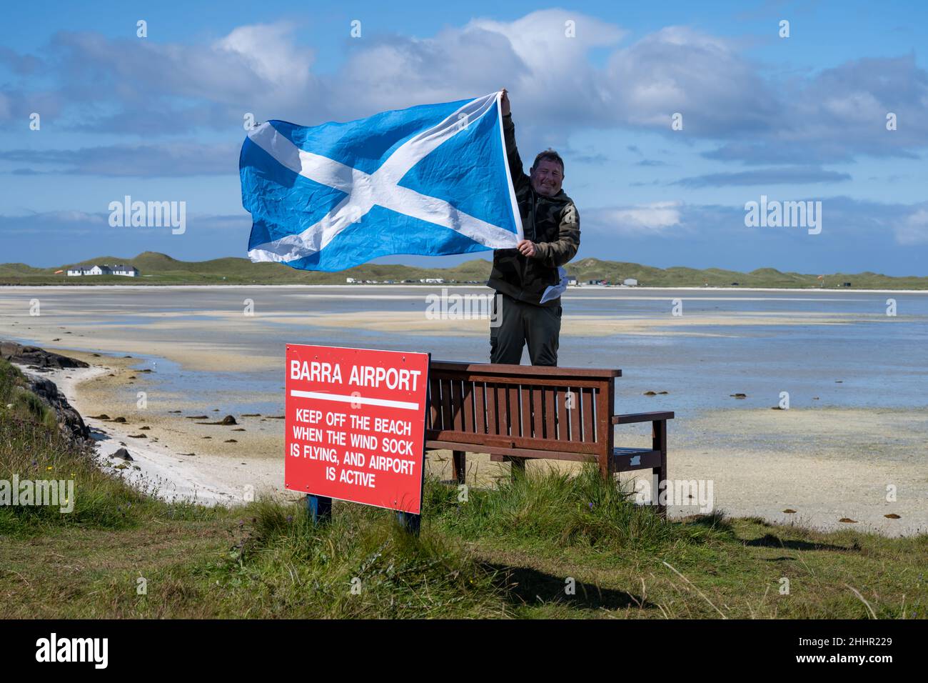 A visitor holds the Scottish flag at Traigh Mhor Beach (in English 'Big Beach'), Barra Airport, Sound of Barra, Eoligarry Stock Photo