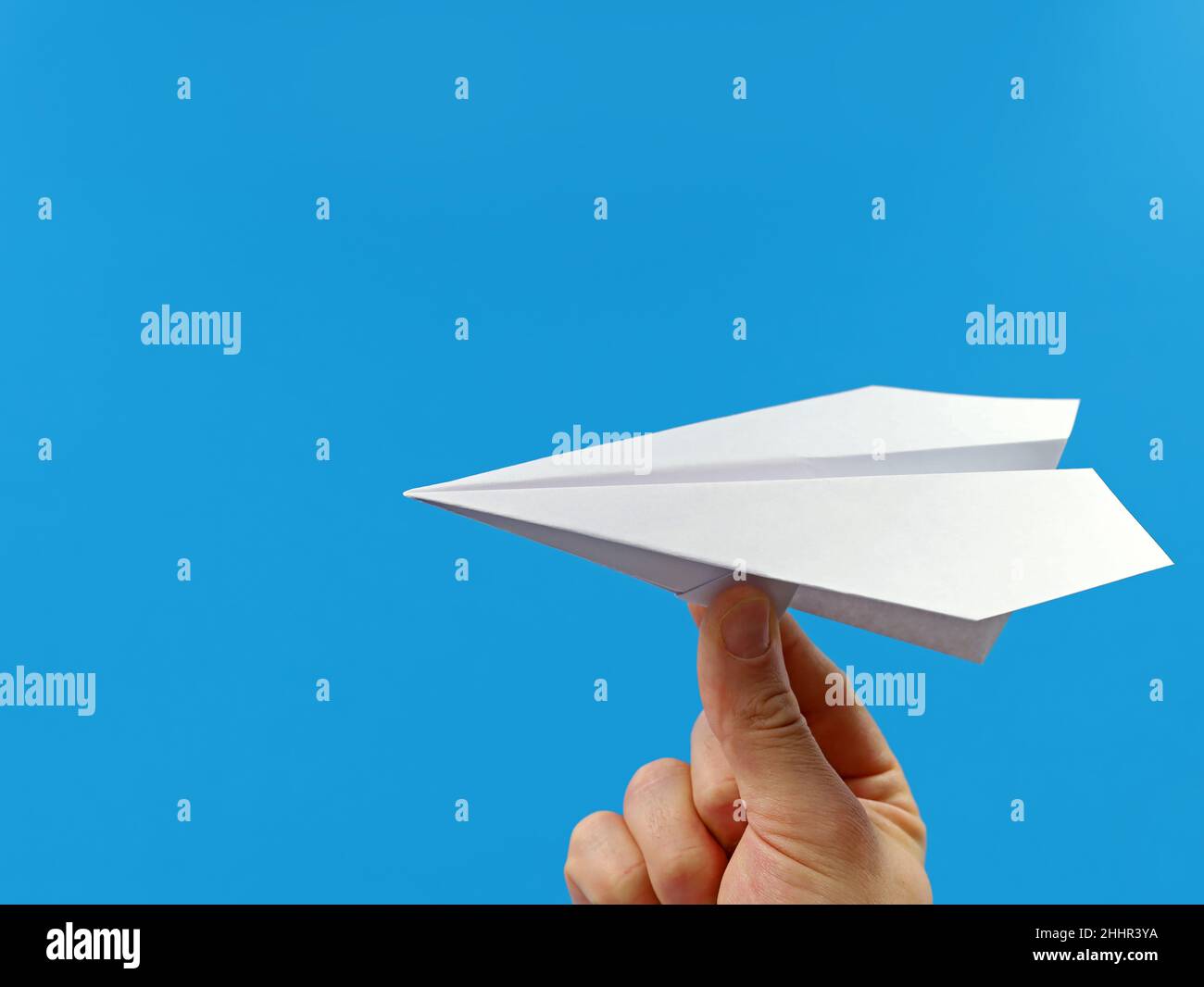 male hand holding paper plane isolated on blue background with copy space Stock Photo