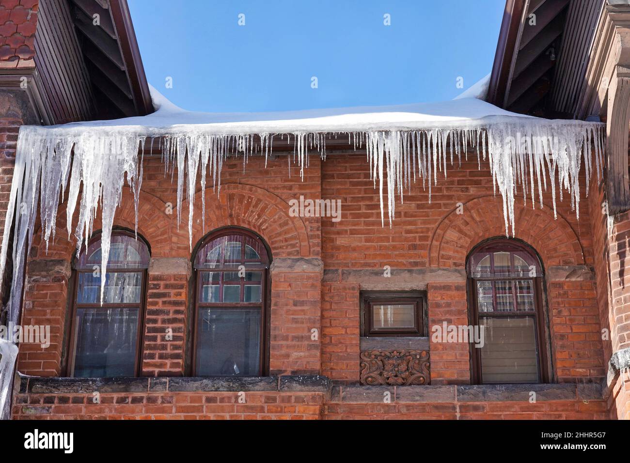 Old brick house with large icicles hanging from the roof Stock Photo