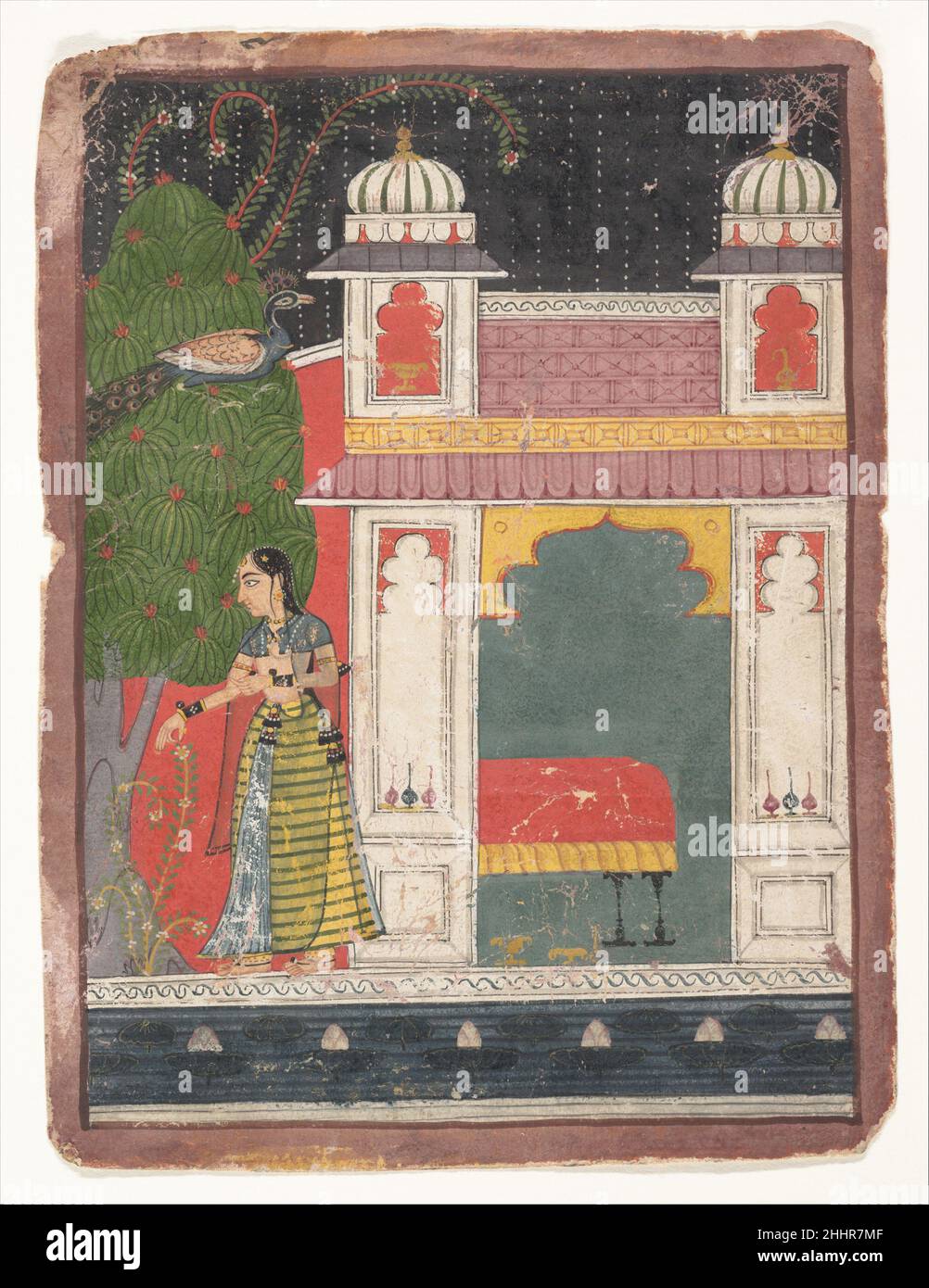 A Heroine Plucking a Flower: Page from a Dispersed Nayikabheda ca. 1660–80 India (Madhya Pradesh, Malwa) The artist instilled this painting with an iconography of longing: the empty bed, the solitary nayika (heroine), and the forlorn call of the peacock. The patterned raindrops, stylized creepers, and surface treatment of the architecture distinguish this manuscript from other work done in the Malwa courts. The figural type suggests an awareness of the Mewar or Bundi traditions; the use of a black sky and a red color field behind are typical of the archaic tastes of Malwa production, which sur Stock Photo