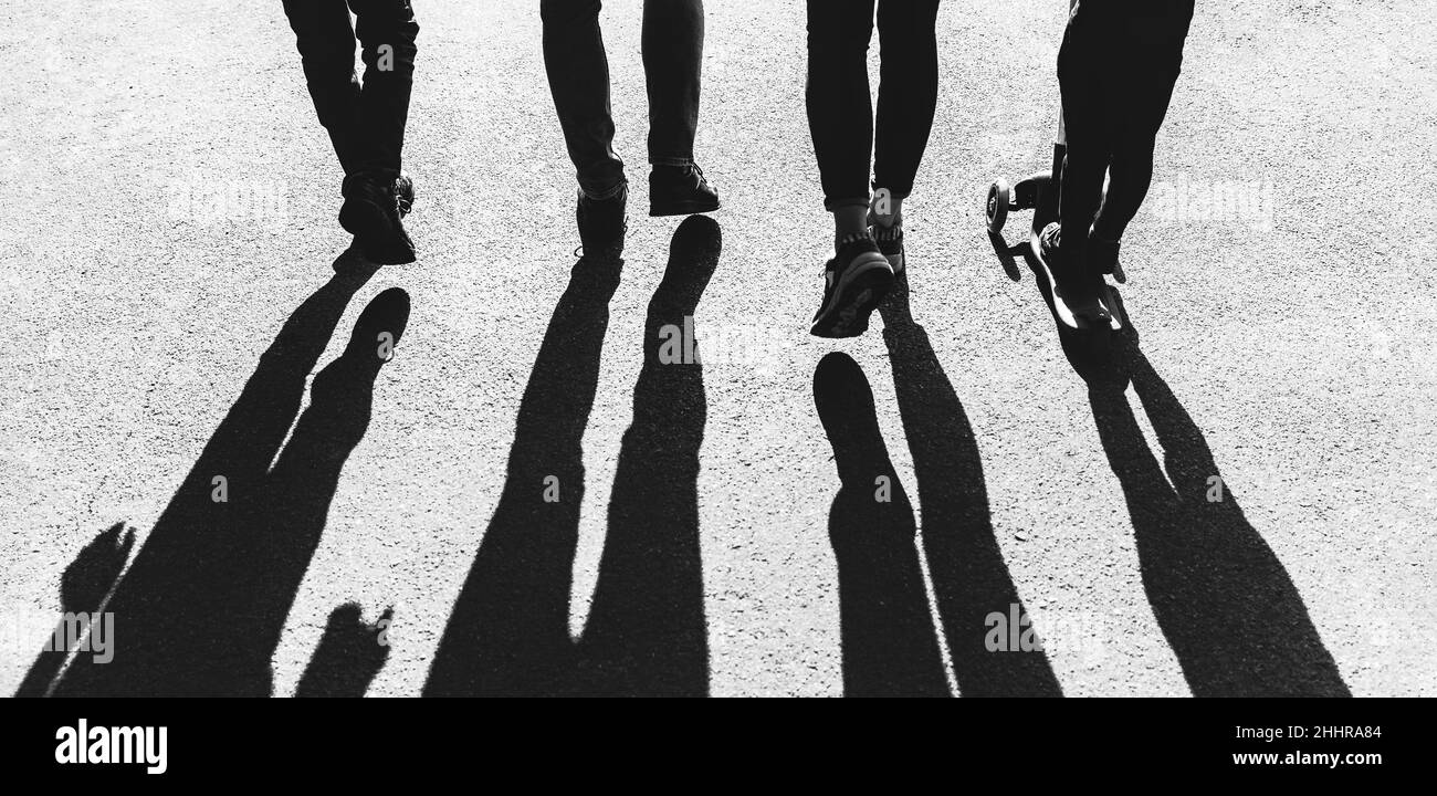 Silhouettes of young people in the backlight. Young family dad, mom and two children walk along the path in the park in the rays of the setting sun Stock Photo